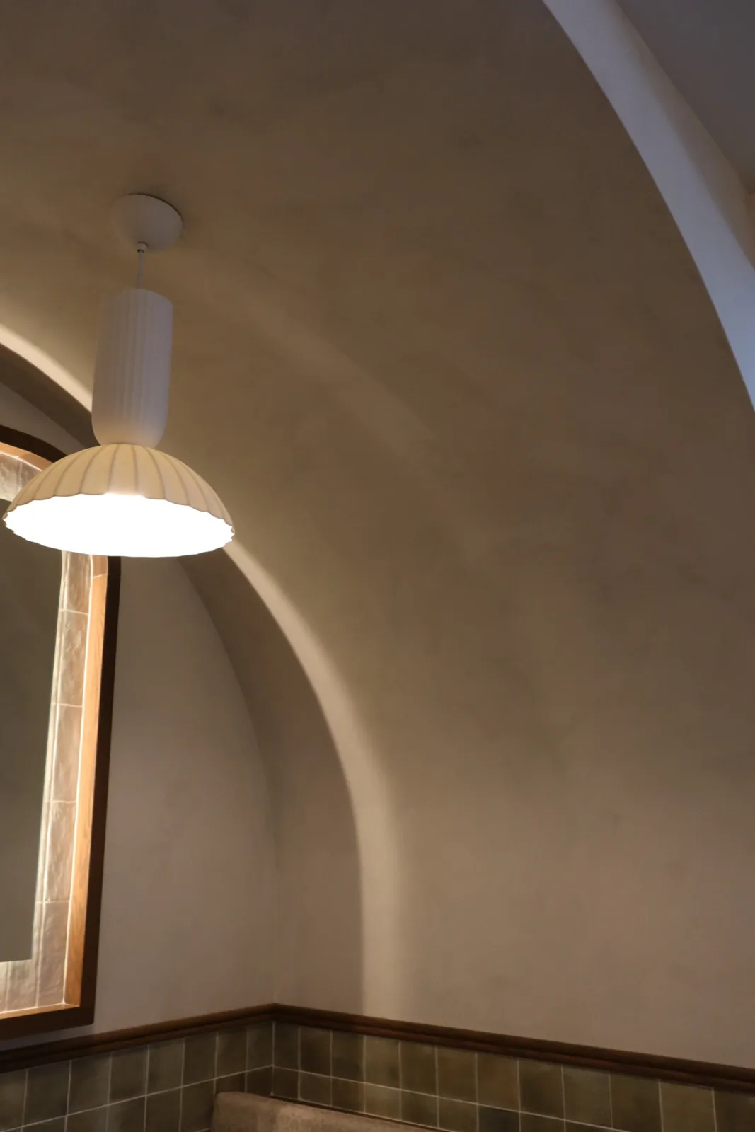 Curved limewash ceiling cove framing an arched mirror and fluted pendant light at Cocotte Bistro, Ottawa