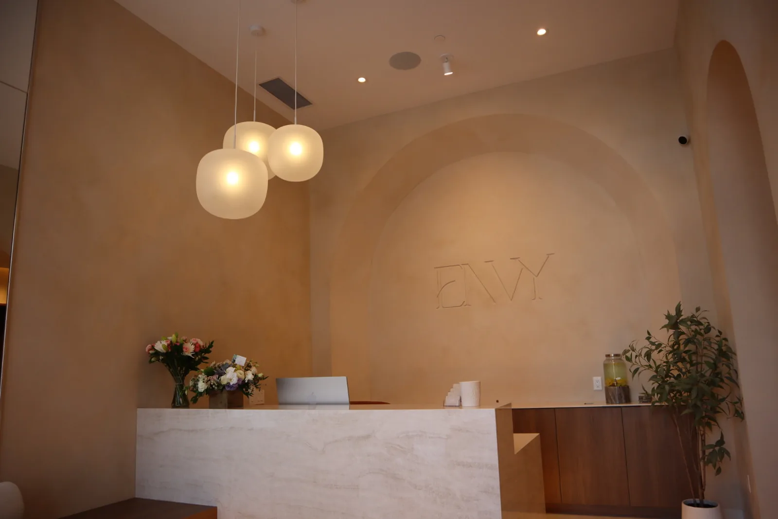 Travertine reception desk in front of a limewash arch wall with embossed ENVY logo at Envy Cosmetic Clinic, Ottawa