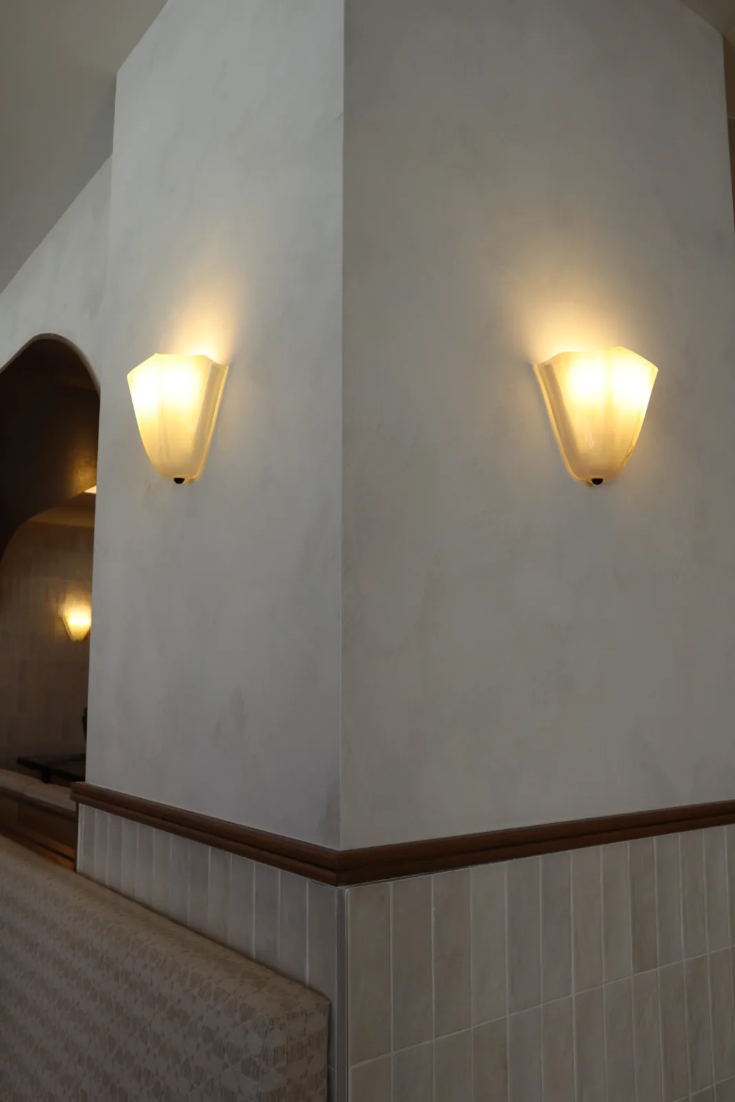 Twin alabaster sconces on a limewashed column corner beside arched openings at Cocotte Bistro, Ottawa