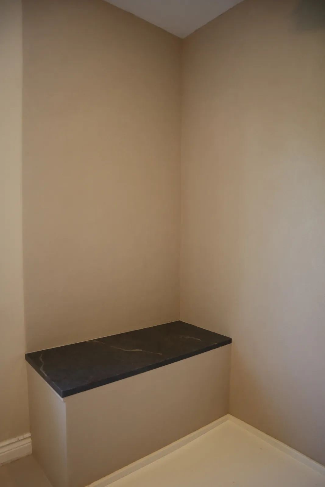 Warm greige bench nook with dark stone cap in a Kanata ensuite finished in microcement