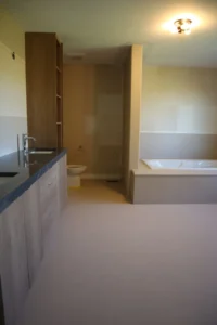 Seamless warm greige microcement floor over existing tile in a Kanata master ensuite with new oak vanity